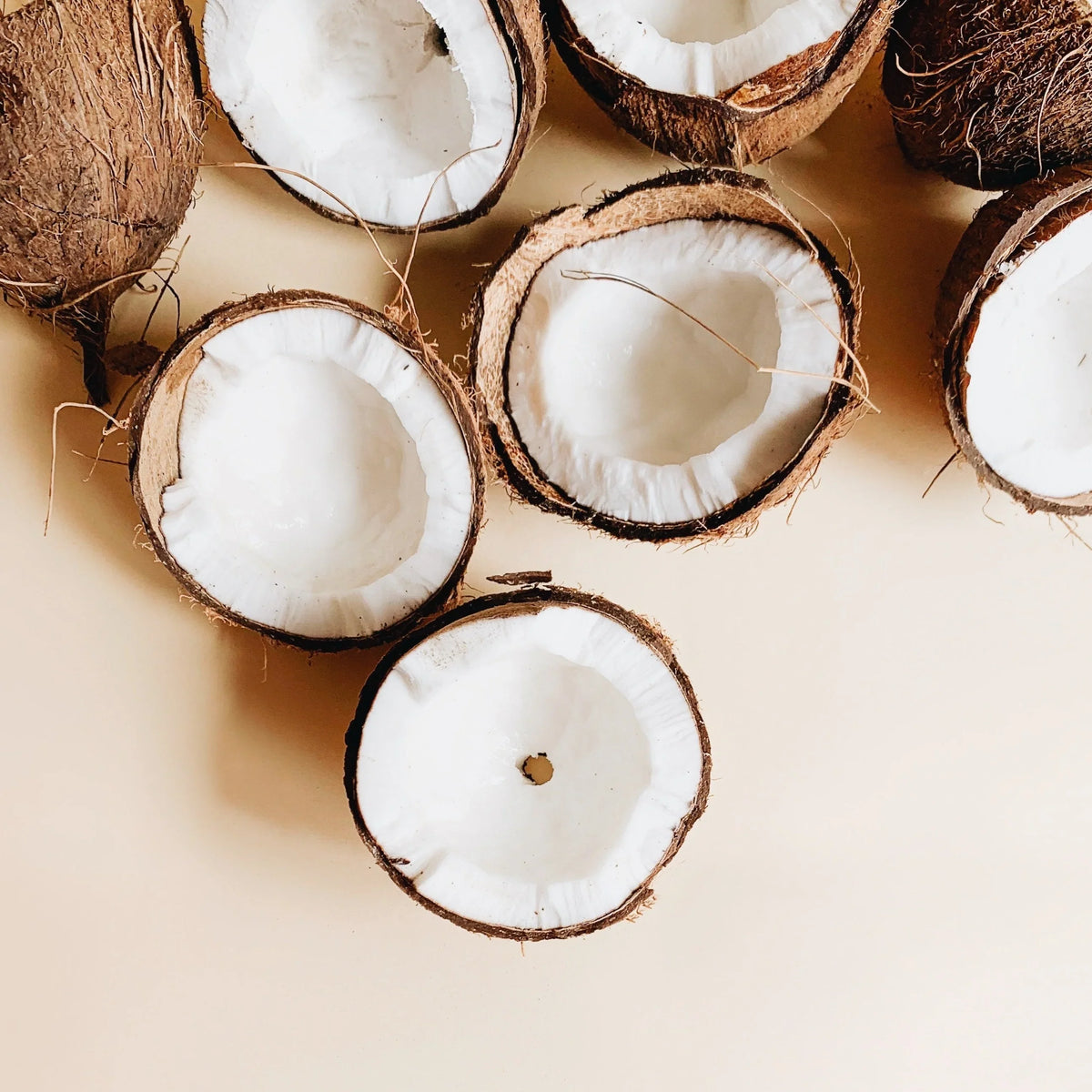 Halved coconuts with white flesh on beige background, fresh coconut shells closeup