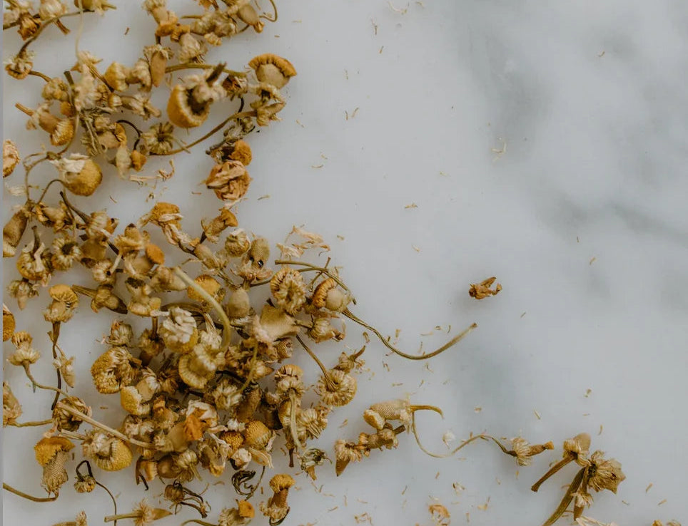 Loose dried chamomile flowers spread on a white marble surface