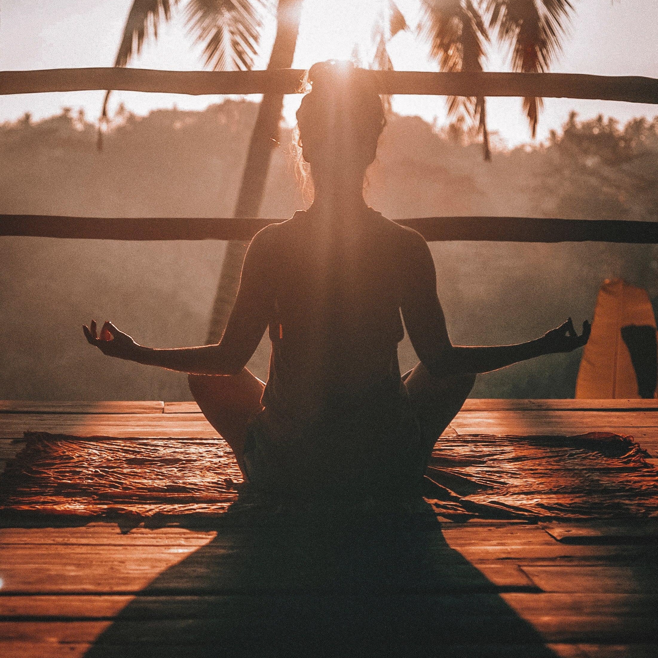 Woman meditating at sunrise on wooden deck with palm trees in tropical setting