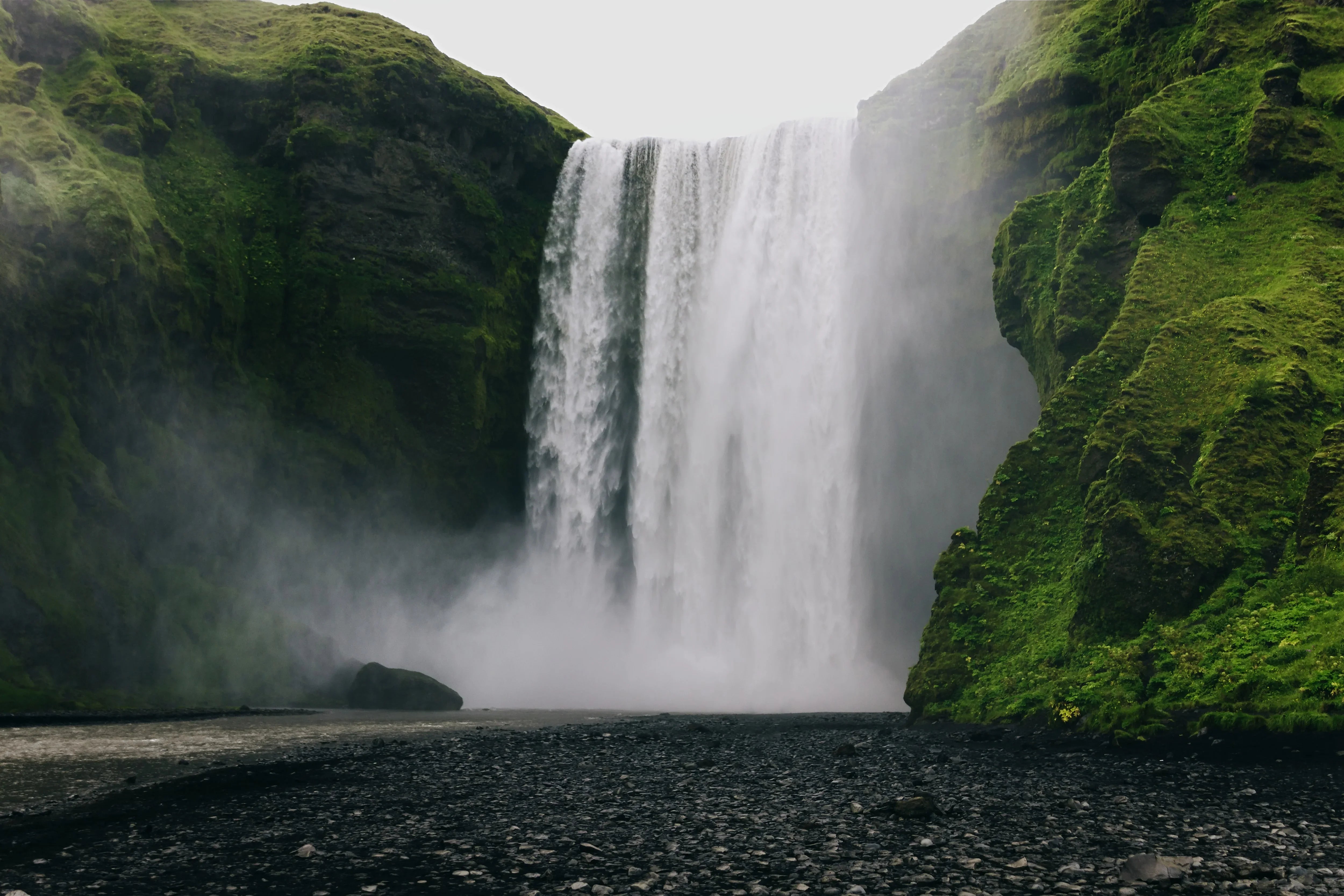 Powerful waterfall cascading over mossy cliffs with rocky black sand foreground