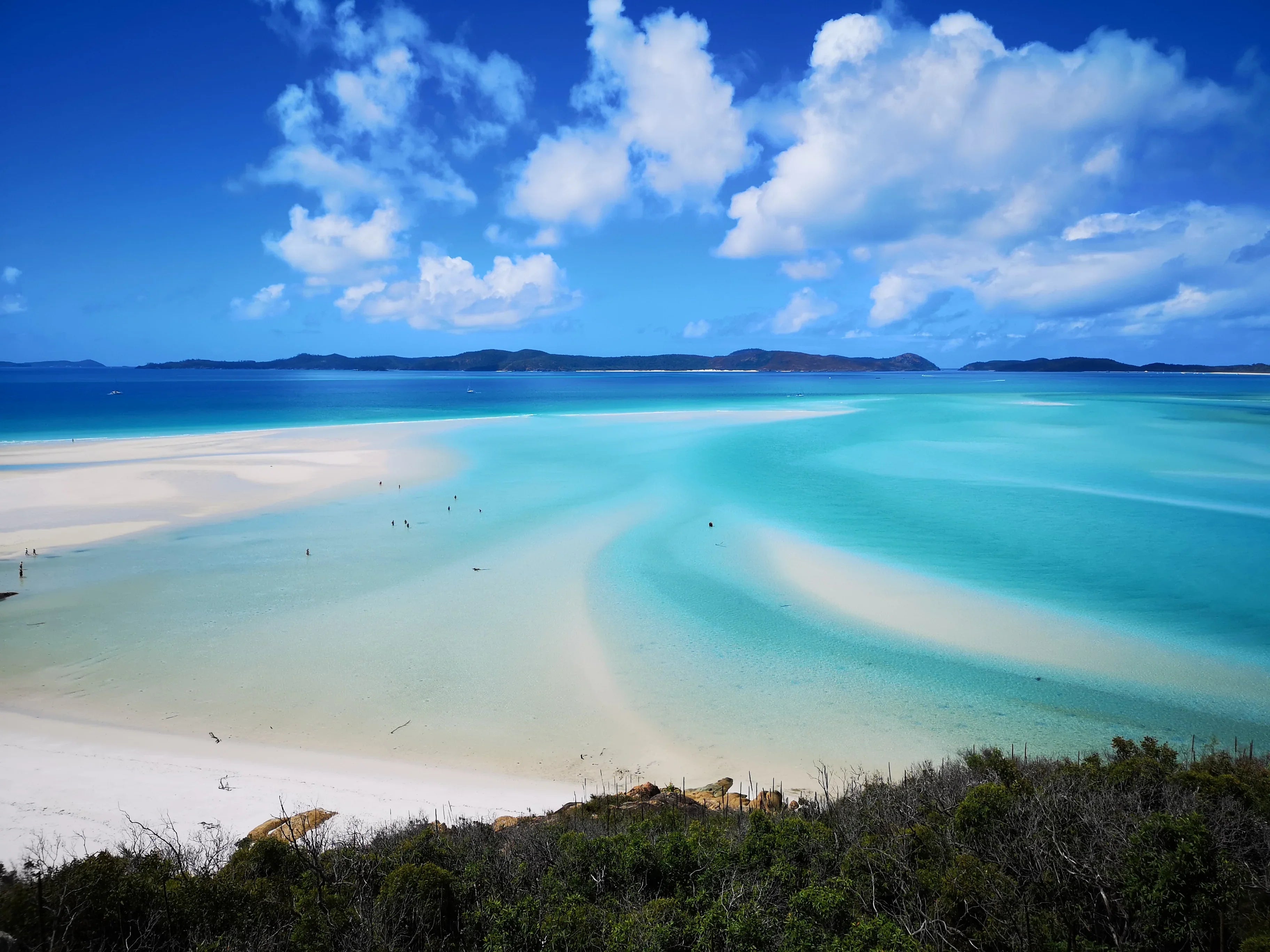 Clear blue ocean, white sand beach, and distant islands under a sunny sky