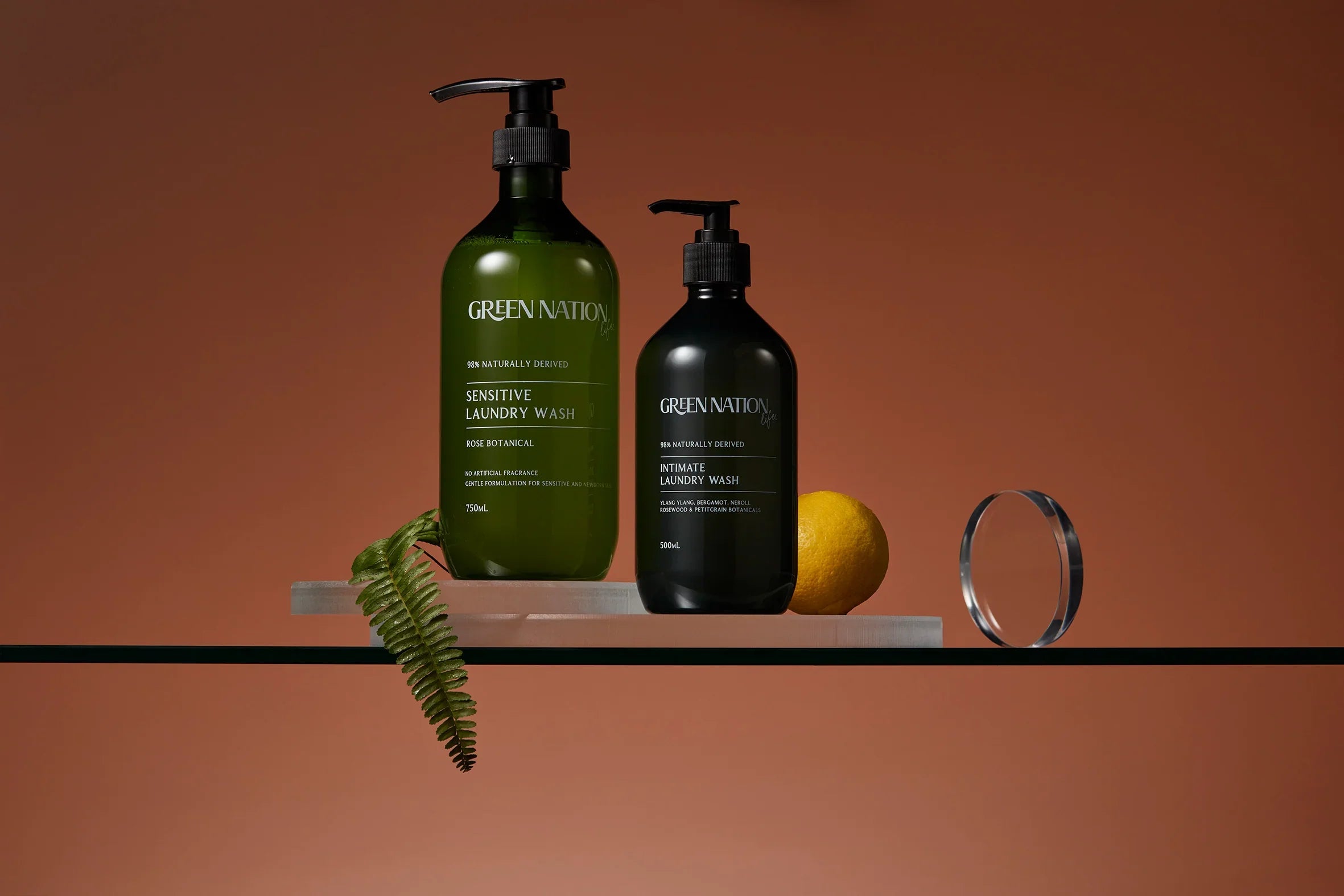 Green Nation laundry wash bottles with lemon and fern on glass shelf, brown background