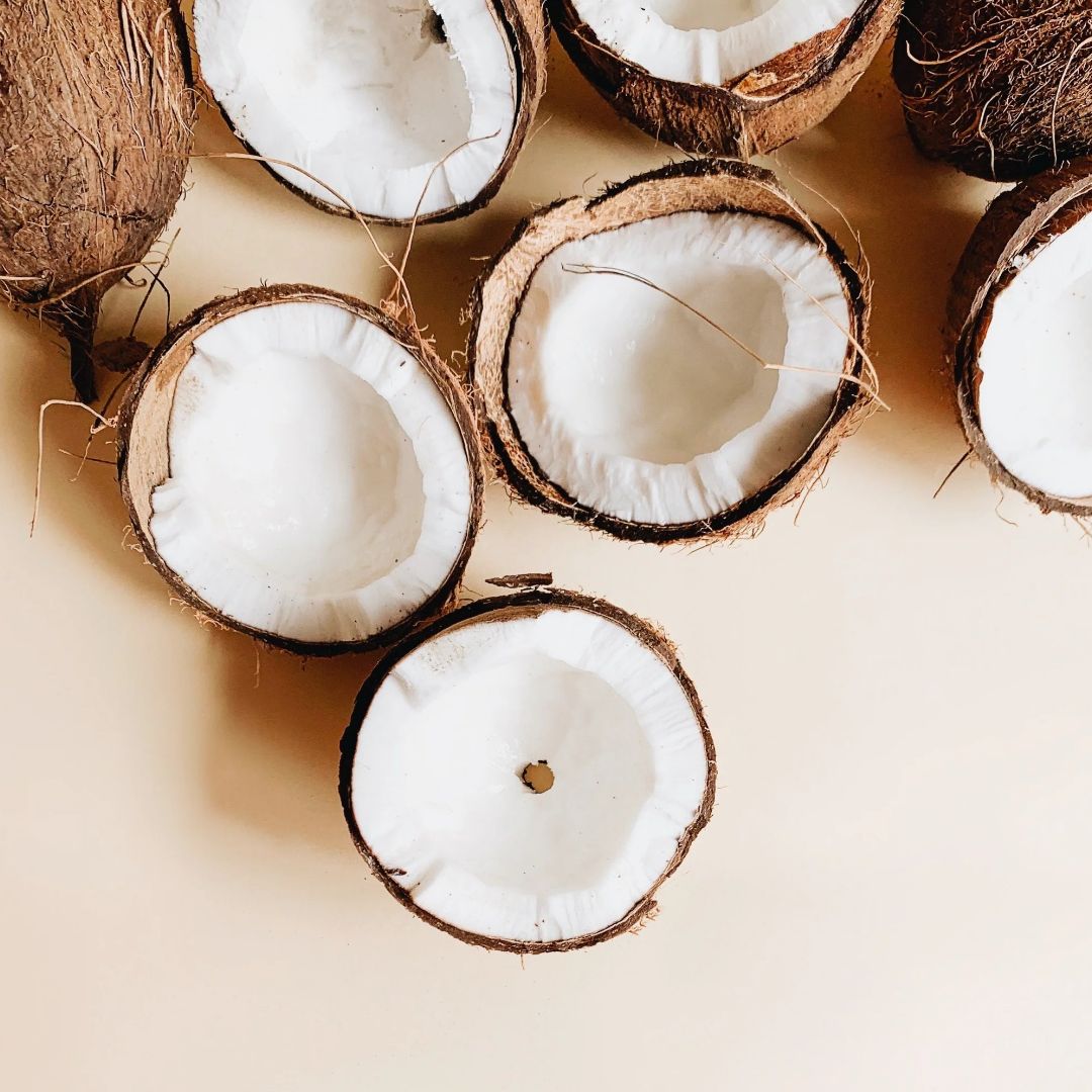 Fresh halved coconuts on a light beige background, showing white coconut meat