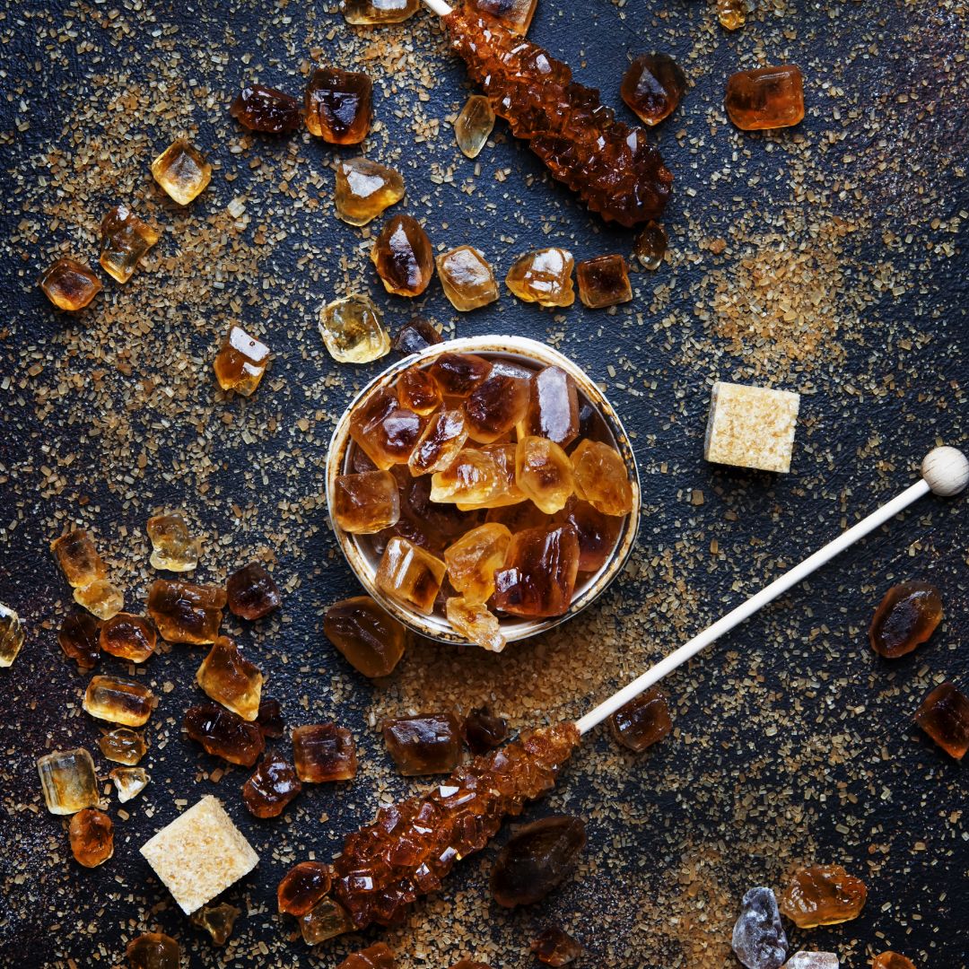 Salted caramel rock sugar pieces in a bowl, with brown sugar cubes and crystals on a dark surface.