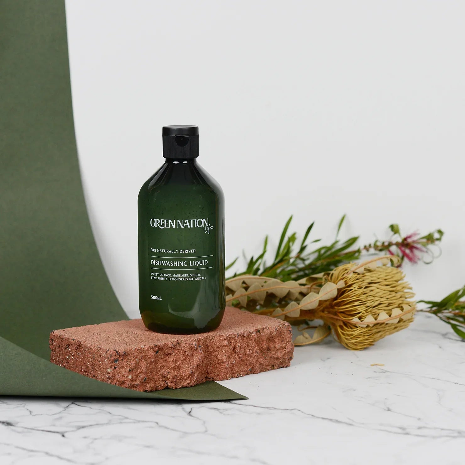 Green Nation Life dishwashing liquid bottle on a brick with flowers and green backdrop