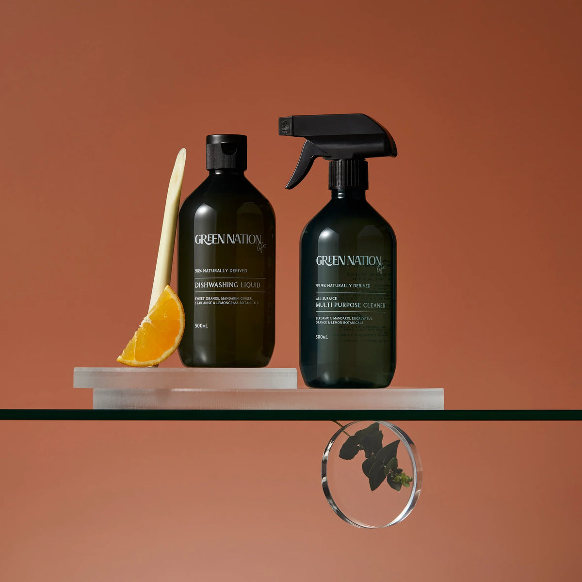 Green Nation dishwashing liquid and multi-purpose cleaner bottles on glass shelf with orange and lemongrass