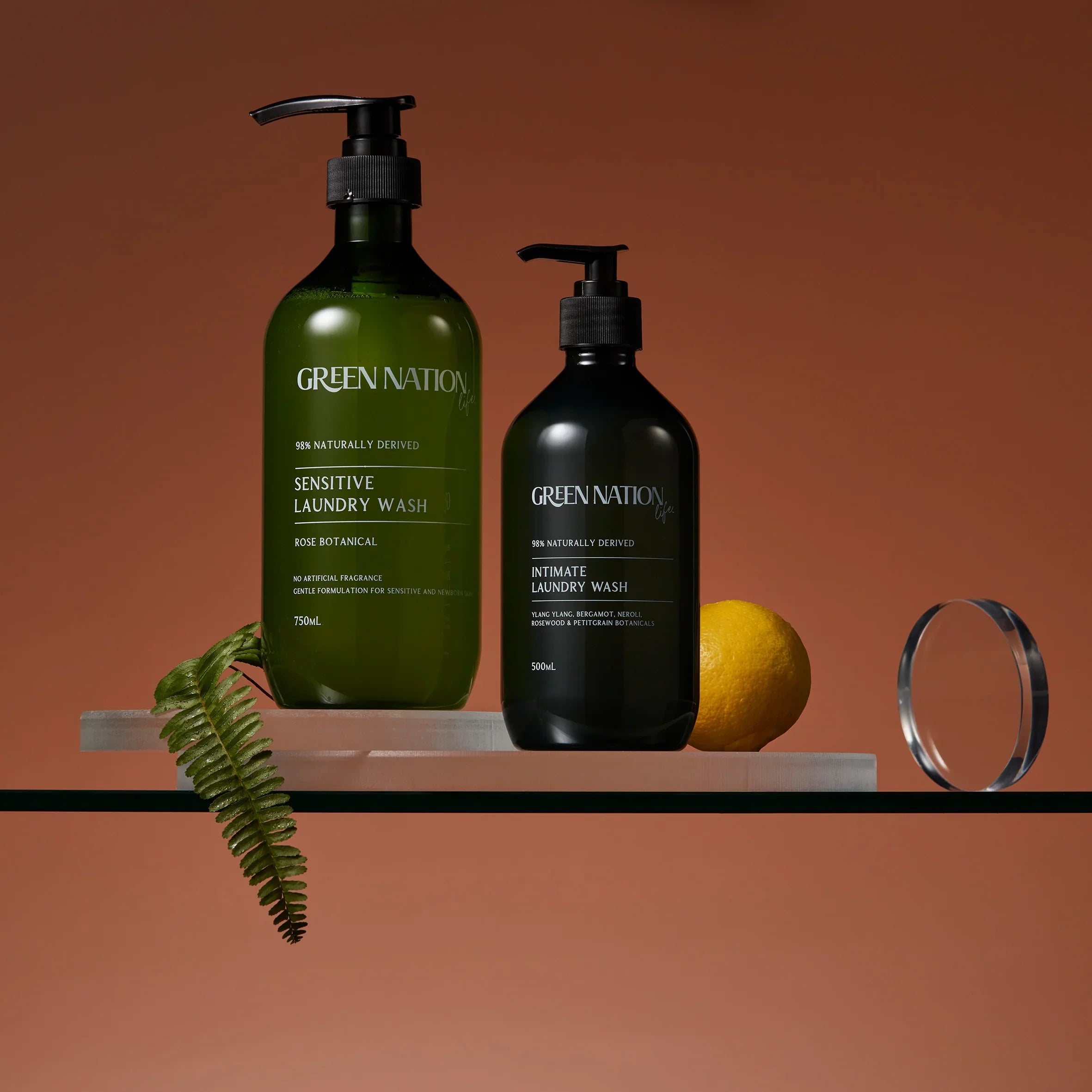 Green Nation laundry wash bottles, lemon, fern, and ring on glass shelf with brown background