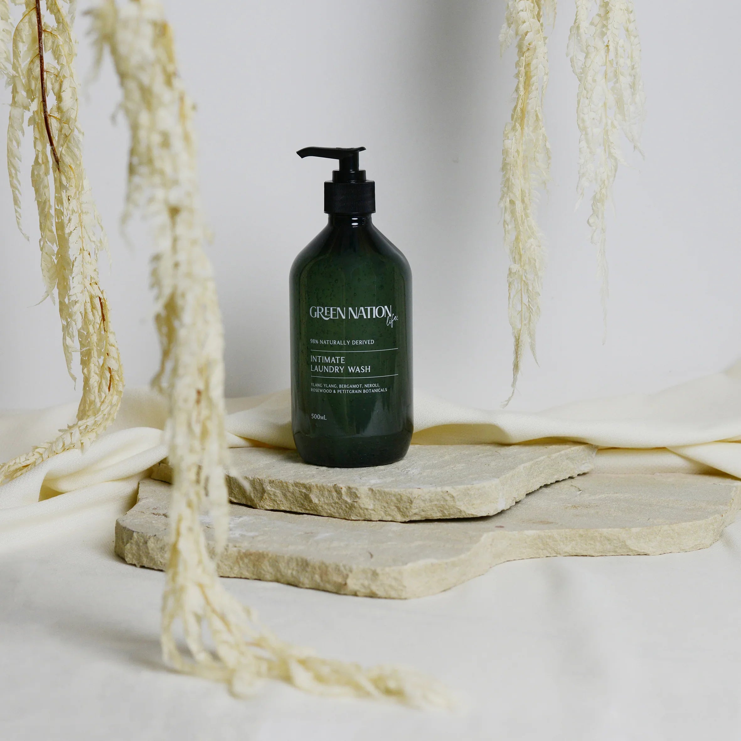 Green Nation Life laundry wash bottle on stone slabs with cream fabric and dried foliage
