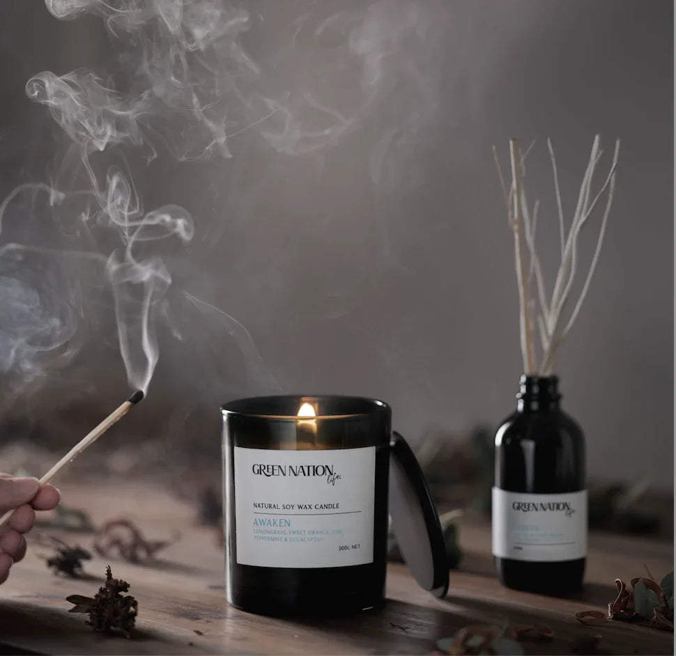 Soy wax candle by Green Nation burning on wooden table with diffuser and smoke from match