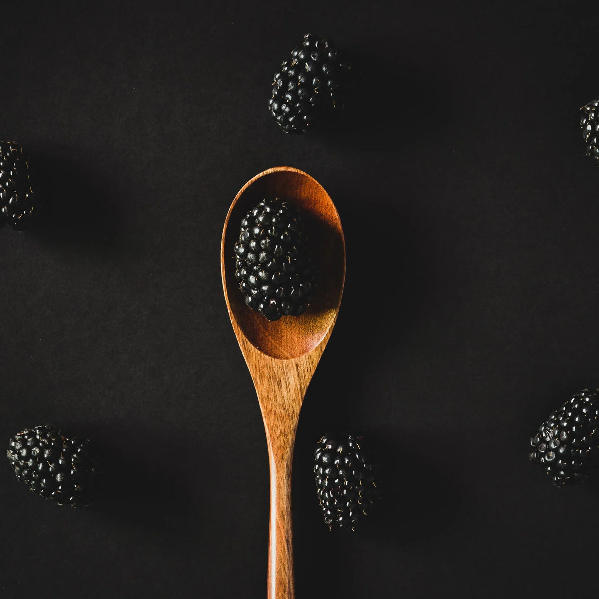 Fresh blackberries on dark background with a wooden spoon