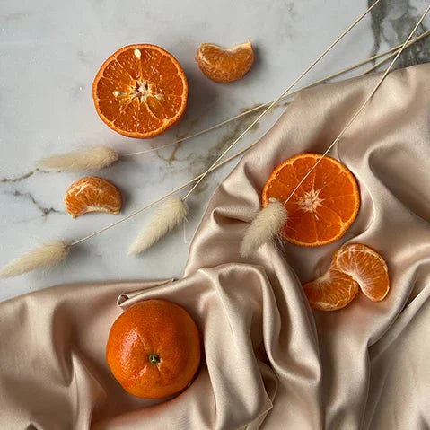 Fresh tangerines and slices on marble with beige silk fabric and dried pampas grass